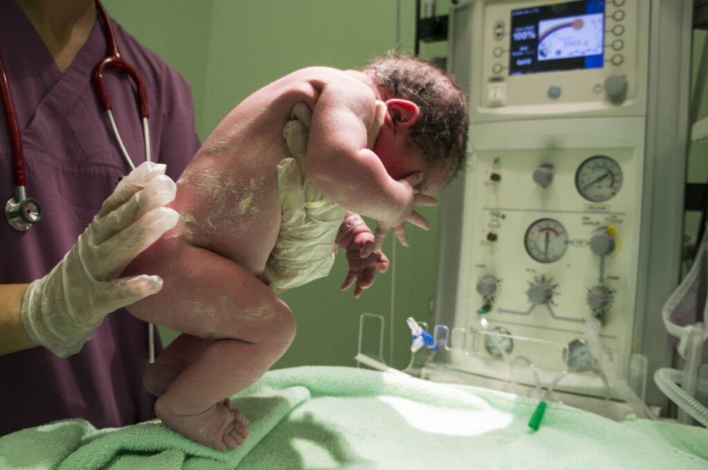 Een verpleegster die een pasgeboren baby vasthoud voor onderzoek na de geboorte